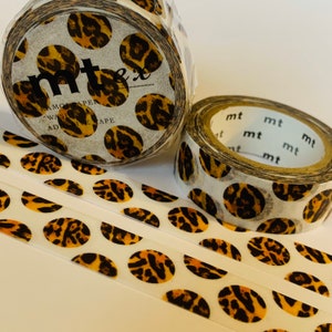 May include: Three rolls of washi tape with a leopard print pattern. The tape is white with brown and orange leopard spots. The tape is labeled "mt" and "mt ex washi tape".