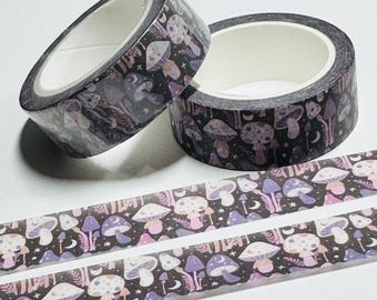 Puede incluir: Dos rollos de cinta adhesiva decorativa con un diseño de setas en tonos morados, rosas y blancos sobre fondo negro. Dos tiras de la misma cinta están desenrolladas debajo. La cinta es adecuada para manualidades y scrapbooking.