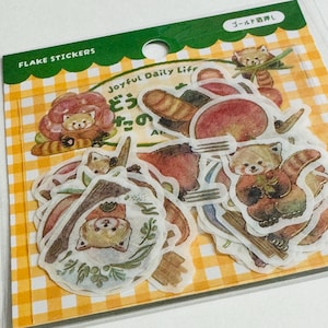 May include: A pack of flake stickers featuring illustrations of red pandas and food items. The stickers have a watercolor style with a variety of shapes and sizes. The packaging includes the text "FLAKE STICKERS" and "Joyful Daily Life".