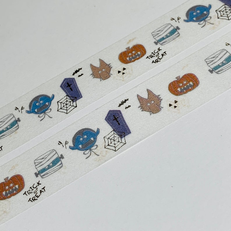 Puede incluir: Cinta washi blanca con tem&aacute;tica de Halloween. La cinta presenta un patr&oacute;n repetitivo de momias, calabazas, murci&eacute;lagos, fantasmas y una telara&ntilde;a. El texto "Trick or Treat" est&aacute; impreso en la cinta.