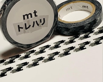 May include: Two rolls of decorative washi tape. One roll is sealed and labeled with the text "mt トレハリ". The other roll is unsealed. The tape has a black and gray geometric pattern. Strips of the patterned tape are visible.