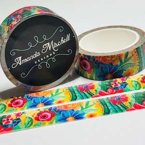May include: Floral patterned washi tape rolls with a black label that reads "Amanda Mischell Designs". The tape features a colorful design of flowers and leaves in shades of red, blue, and yellow. The tape is approximately 15mm wide.