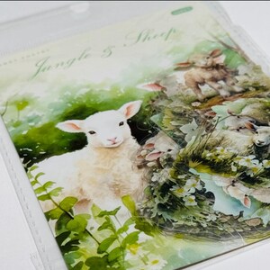 May include: A watercolor illustration featuring a white lamb in a field of green foliage and white flowers. The artwork is titled "Jungle & Sheep" and depicts several sheep in a pastoral scene. The image is in a clear plastic sleeve.