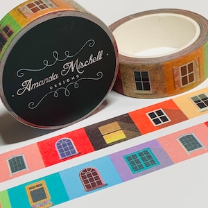 May include: A roll of washi tape featuring a repeating pattern of colorful windows with different styles and frames. The tape is packaged on a black spool with the text "Amanda Mischell Designs" in white cursive lettering.