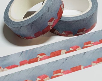 Puede incluir: Dos rollos de cinta washi con un patrón repetido de casas rojas y un cielo azul claro. La cinta está sobre una superficie blanca.