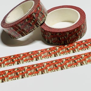 May include: Two rolls of decorative washi tape with a repeating pattern of red and white mushrooms on a brown background. Two strips of the same tape are unrolled below the rolls. The tape is designed for crafts, scrapbooking, and other creative projects.