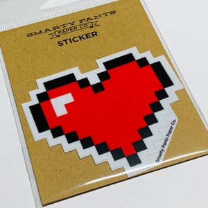 May include: A red pixelated heart sticker with a black outline. The sticker is on a brown background with the text "SMARTY PANTS PAPER CO. STICKER" above it.