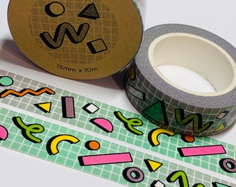 Puede incluir: Dos rollos de cinta washi con un patrón de cuadrícula verde y formas geométricas de colores. La cinta está etiquetada como "RAD WASHI TAPE" y "15mm x 10m".