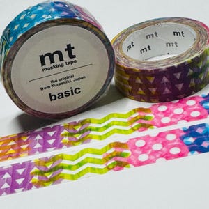 May include: Two rolls of masking tape with colorful geometric patterns. One roll has a label that reads "mt masking tape" and "basic". The other roll has a pattern of triangles. Two strips of tape with zig-zag and polka dot patterns are also visible.