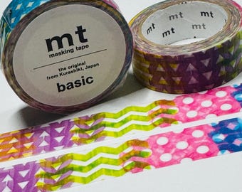 Puede incluir: Dos rollos de cinta adhesiva decorativa con patrones geométricos coloridos. Un rollo tiene la etiqueta "mt masking tape" y "basic". El otro rollo tiene un diseño de triángulos. También se ven dos tiras de cinta con patrones en zigzag y lunares.