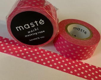 Puede incluir: Dos rollos de cinta adhesiva washi rosa con lunares blancos y una tira de la misma cinta. Un rollo está envuelto en plástico transparente y tiene una etiqueta negra con texto blanco que dice "masté washi masking tape".