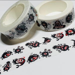 May include: Two rolls of decorative washi tape featuring a repeating pattern of cartoon monsters in black, gray, and red. The tape is white with the monster designs wrapping around the rolls and printed on the unrolled tape.