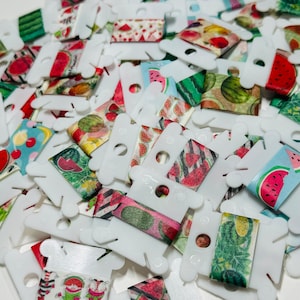May include: A collection of colorful washi tapes featuring watermelon, fruit, and floral patterns. The tapes are wound around white plastic spools.