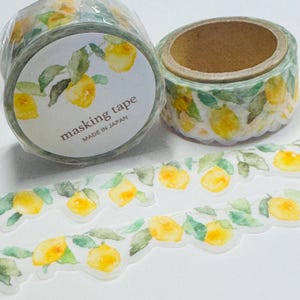 May include: Two rolls of masking tape with a watercolor lemon design. The tape is labeled "masking tape MADE IN JAPAN". The lemons are yellow with green leaves. A strip of the tape is unrolled, showing the lemon pattern.