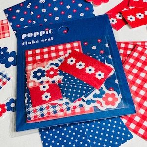 May include: A pack of Poppie flake seal stickers in a blue plastic sleeve. The stickers feature red and blue patterns including gingham, polka dots, and small white or red flowers. Several loose stickers are scattered around the main package.