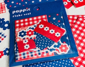 May include: A pack of Poppie flake seal stickers in a blue plastic sleeve. The stickers feature red and blue patterns including gingham, polka dots, and small white or red flowers. Several loose stickers are scattered around the main package.