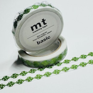 May include: Two rolls of masking tape with a green clover pattern. The tape is labeled "mt masking tape basic" and is from Kurashiki, Japan. A length of the tape is unrolled, showing the clover design.