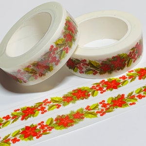 May include: Two rolls of decorative washi tape featuring a Christmas poinsettia and holly berry design. The tape is white with a repeating pattern of red flowers, green leaves, and red berries. Two strips of the tape are unrolled.