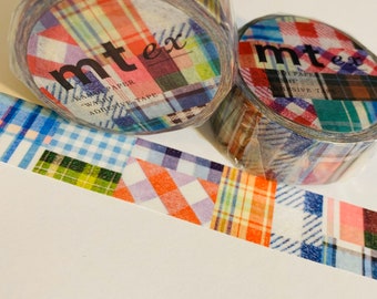 Puede incluir: Dos rollos de cinta washi mt ex con un diseño de cuadros de patchwork en tonos de azul, naranja, verde y rojo. La cinta está parcialmente desenrollada, revelando una tira de cinta adhesiva estampada. El texto "mt ex" y "washi adhesive tape" son visibles.