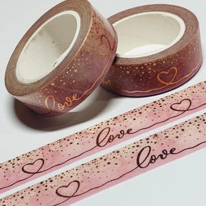 May include: Two rolls of decorative washi tape with a pink and brown gradient design, gold stars, and the word "Love" in gold script. Two strips of tape with the same design are also visible.
