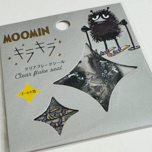 May include: A package of Moomin clear flake seals. The package is silver with Japanese text and illustrations of Moomin characters. Two star-shaped seals are visible, one with a floral design and the other with a bow.