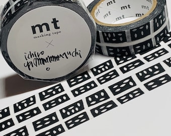 Puede incluir: Dos rollos de cinta washi con estampado en blanco y negro. La cinta presenta un patrón repetitivo de pequeños óvalos blancos dentro de rectángulos negros. La cinta está etiquetada como "mt masking tape" e "ichiro mauchi".