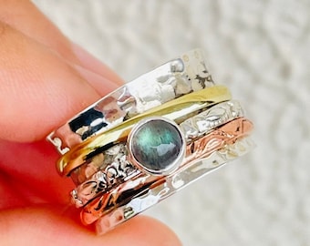 May include: A silver, gold, and copper spinning ring with a green gemstone. The ring is made of multiple bands that spin around each other.