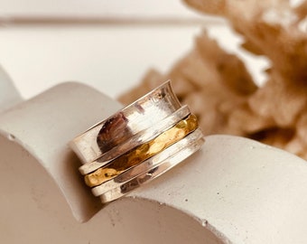 May include: A silver and gold spinning ring with a hammered texture. The ring is made of multiple bands that spin around each other.