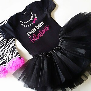 May include: A black bodysuit with the text "I was born fabulous" in pink glitter. The bodysuit is paired with a black tulle tutu and zebra print leggings with pink ruffles.