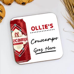 May include: A square white coaster featuring the text "Ollie's Cruzcampo Goes Here" in red and black. A graphic of a red and white Cruzcampo beer can is on the left. The coaster is on a white surface.