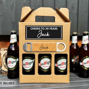 May include: A cardboard beer carrier with a handle, holding three San Miguel beer bottles. The carrier has a black and white label that reads "Cheers to 30 Years Jack". A bottle opener is included. The text "*BEER NOT INCLUDED" is at the bottom.