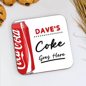 May include: Square coaster featuring a red and white Coca-Cola can design on the left. The coaster has the text "DAVE'S Coke Goes Here" in red and black. The coaster is white with rounded corners.