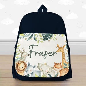 May include: Navy blue backpack with a jungle animal design. The front panel features a watercolor illustration of a lion, giraffe, zebra, elephant, rhino, and fox. The name "Fraser" is written in cursive.