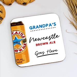May include: Square coaster featuring a Newcastle Brown Ale can design. The coaster reads "GRANDPA'S Newcastle BROWN ALE Goes Here" in blue, red, and black. The coaster is white with a brown edge.