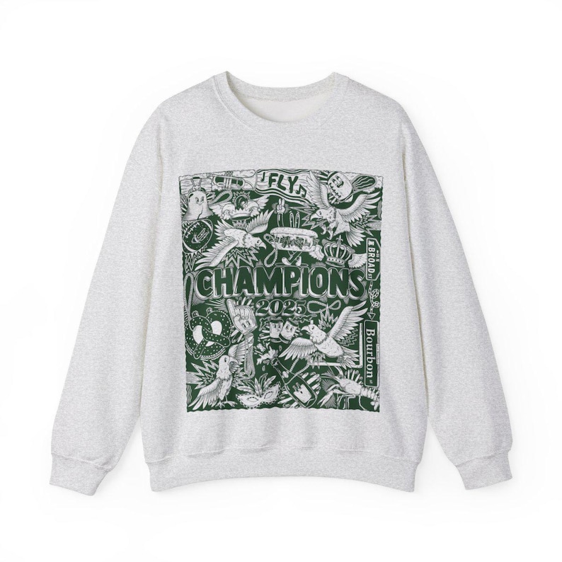 Puede incluir: Una sudadera gris con un estampado gr&aacute;fico verde de varias im&aacute;genes, incluyendo p&aacute;jaros, una corona y el texto "CHAMPIONS 2025".