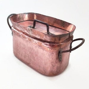 May include: An oval copper pot with a lid and two handles. The pot is made of hammered copper and has a rustic, antique look.