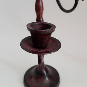 May include: A dark brown wooden candlestick with a single candle holder. The candlestick has a round base and a decorative scroll design.