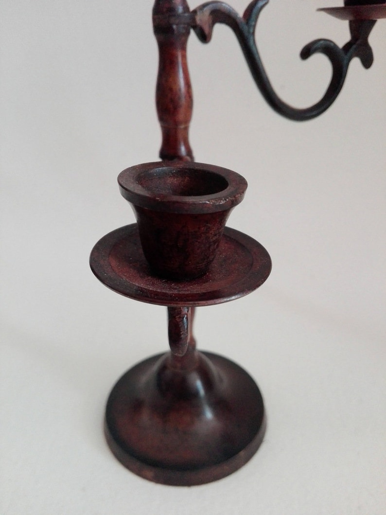 May include: A dark brown wooden candlestick with a single candle holder. The candlestick has a round base and a decorative scroll design.