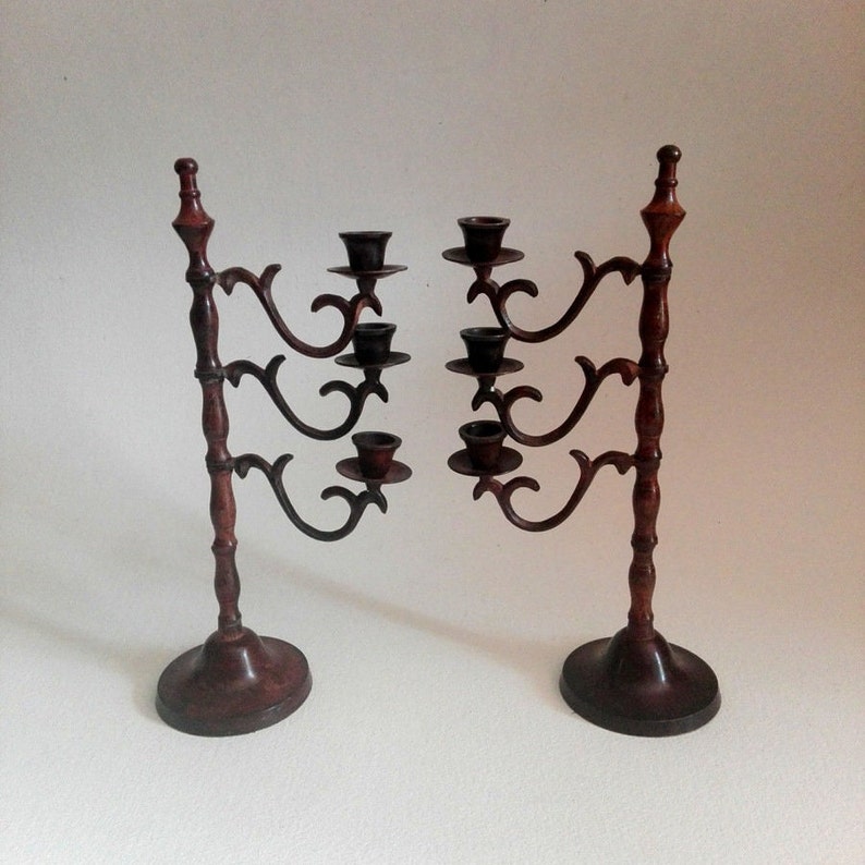 May include: A set of two ornate, dark brown metal candle holders with five candle cups each. The candle holders have a traditional design with intricate details.
