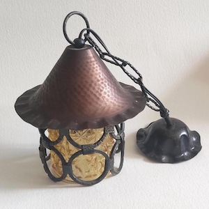 May include: Vintage hanging pendant light with a copper-colored, textured shade and a decorative metal frame. The light fixture has a yellow glass insert and a chain for hanging. The ceiling mount is also included.