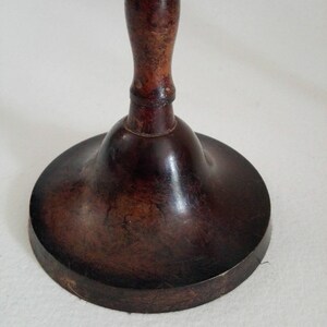 May include: A dark brown wooden candlestick with a bell-shaped base and a turned wooden stem.