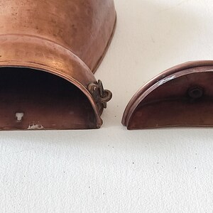 May include: Two copper pieces, one a larger, rounded, open-top container with a hinged lid, the other a smaller, half-circle lid. Both pieces have a worn, aged patina.
