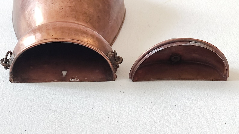 May include: Two copper pieces, one a larger, rounded, open-top container with a hinged lid, the other a smaller, half-circle lid. Both pieces have a worn, aged patina.