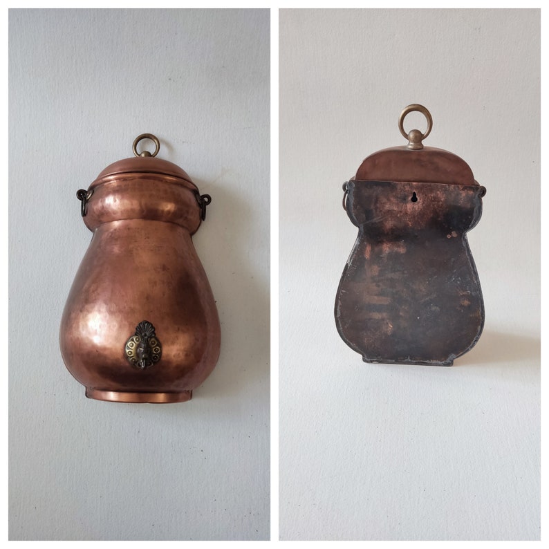 May include: Two copper wall mounted water jugs with a spout and a handle. The jugs are both pear shaped and have a dark patina.