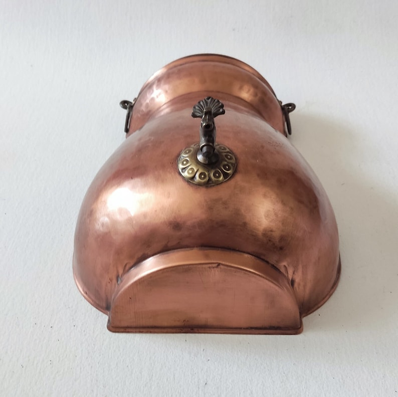 May include: A copper wall mounted water fountain with a decorative spout and a hammered finish.