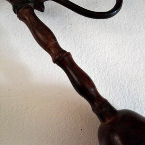 May include: A dark brown wooden bell with a decorative metal handle. The handle is curved and has a floral design.