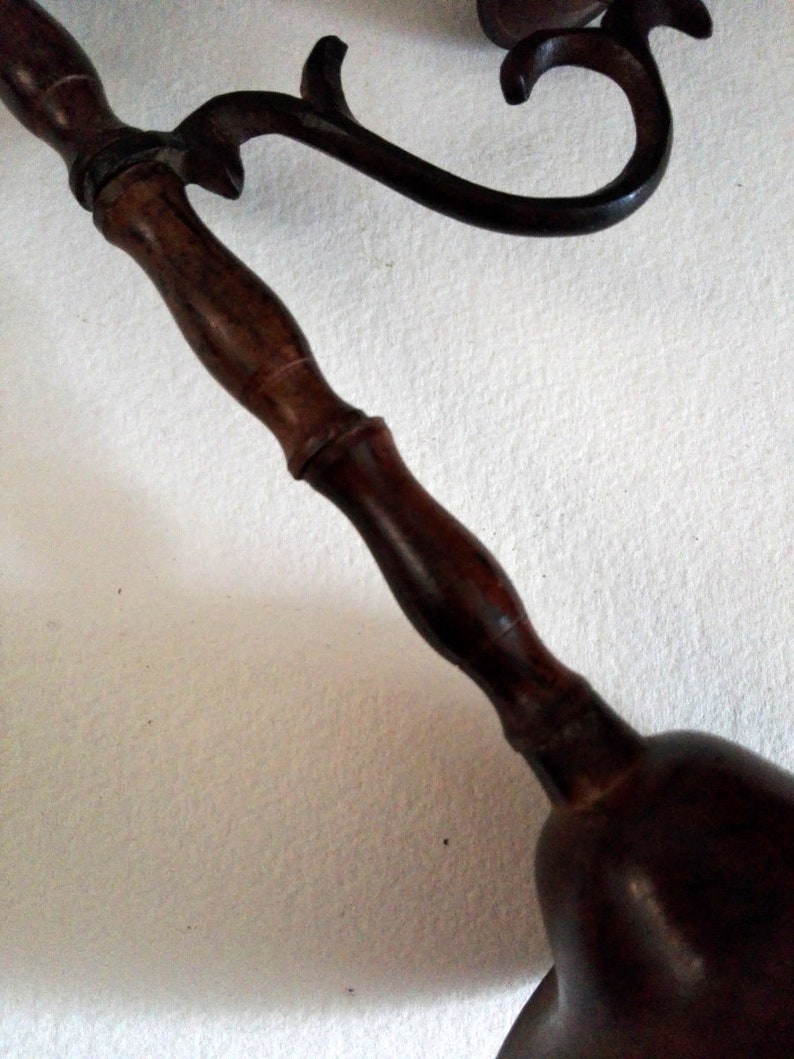 May include: A dark brown wooden bell with a decorative metal handle. The handle is curved and has a floral design.