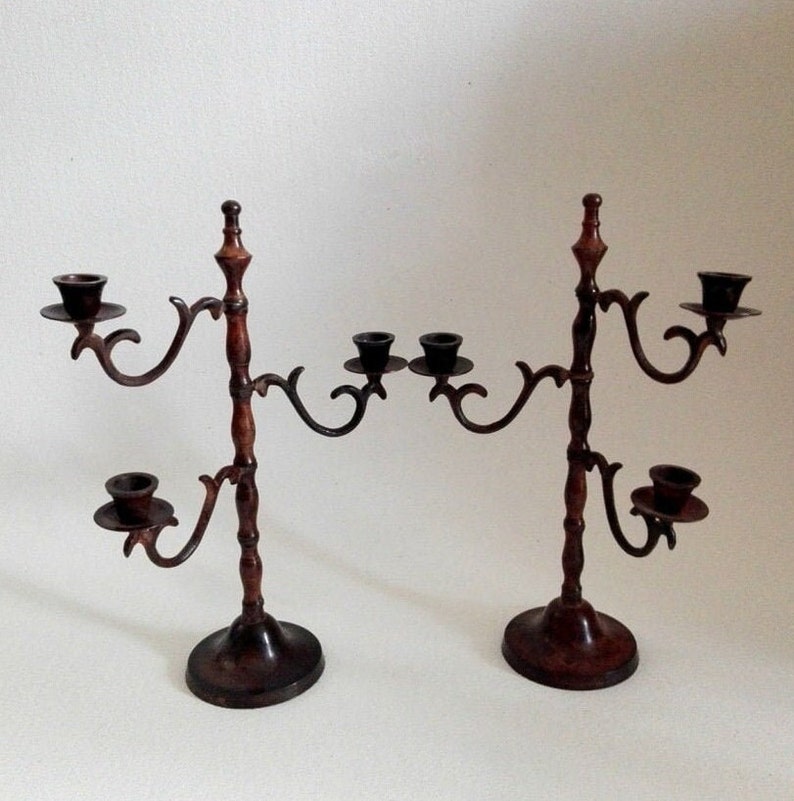 May include: A pair of antique-style, brown metal candle holders with ornate designs. Each holder has five candle arms, with a total of ten candle cups.