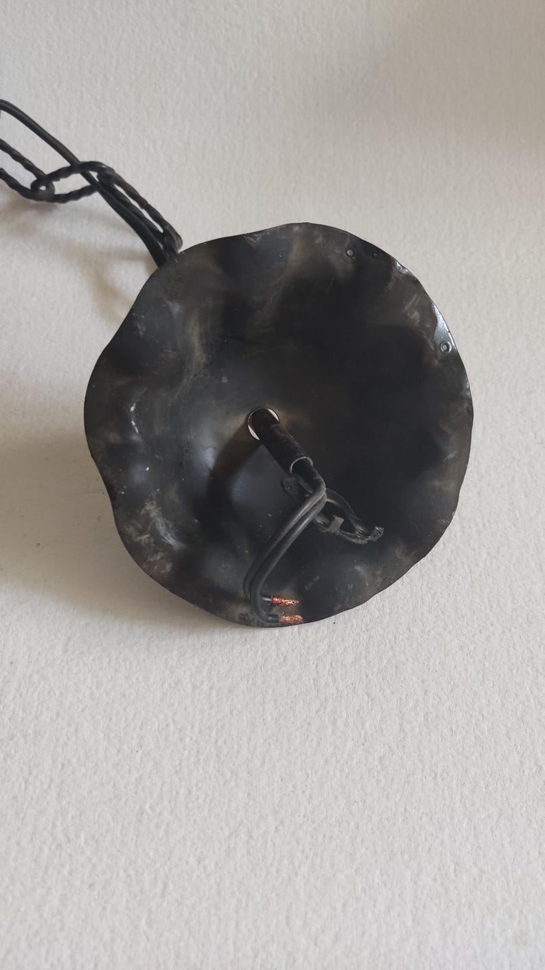 May include: A black, metal ceiling light fixture with a wavy, circular shade. The fixture has a chain for hanging and a wire for electrical connection. The shade has a textured surface and a hole for the light bulb.