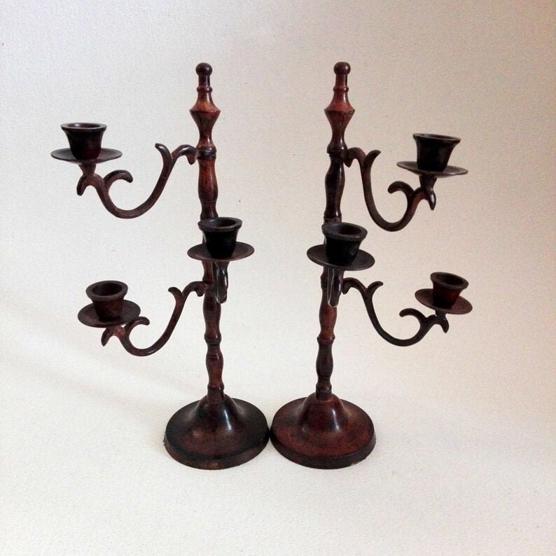 May include: A pair of antique-style, dark brown metal candle holders with ornate designs. Each holder has four candle cups and a decorative base.